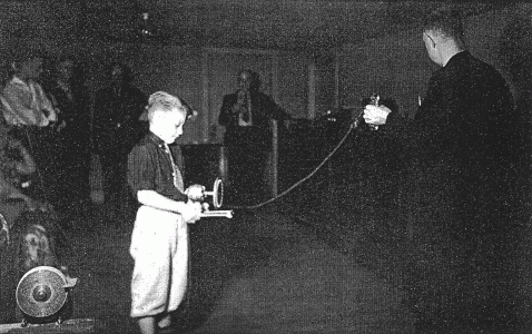 A young boy holds a small electric motor, which is operating from electricity produced by Dr. Moray's device. Moray, right, holds part of his "radiant energy" generating system and an antennae runs down to another man in the far corner. Below on the opposite page a similar demonstration with a powerful light. The electricity actually came from a source picked up by the antennae and converted to useable power.